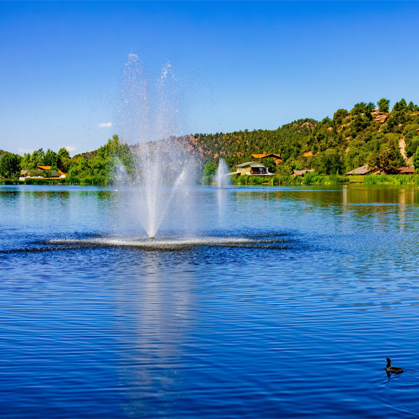 Fountain spraying water in tranquil lake setting with trees and homes in Payson, AZ, symbolizing Ekwall Restoration's commitment to restoring beauty and peace in local environments.