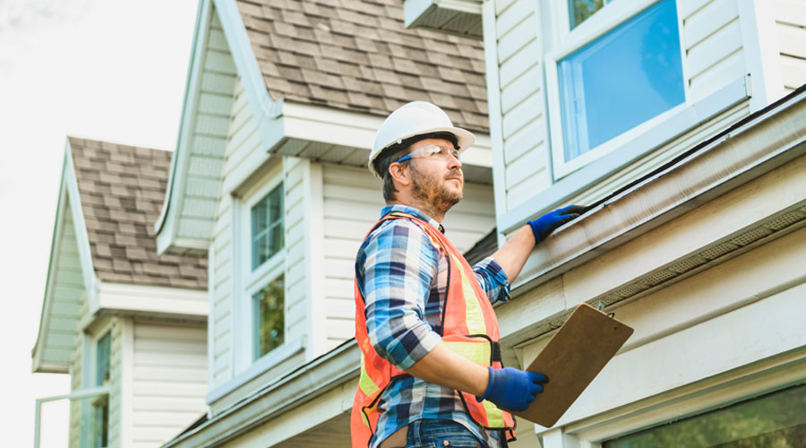 Home restoration expert inspecting roof and gutters, wearing safety gear, clipboard in hand, focused on structural integrity.