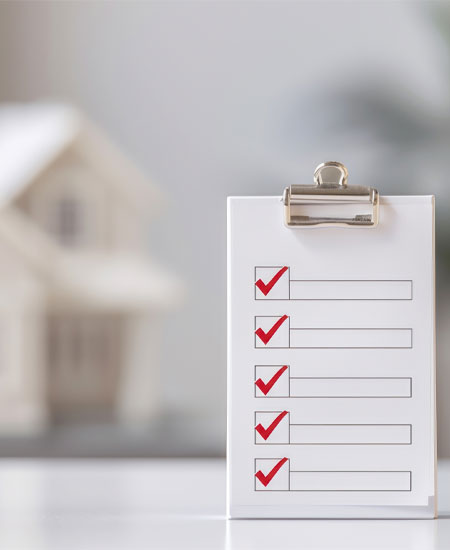 Checklist with checkmarks in front of a blurred model house, symbolizing home restoration planning and assessment.